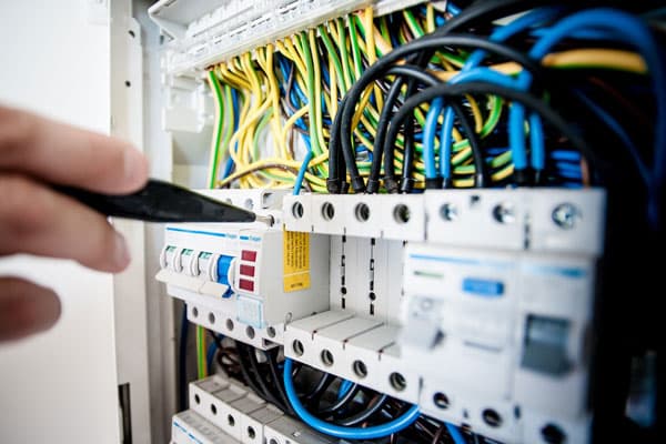 Close-up of a breaker panel with colored wiring and a screwdriver at the breakers.