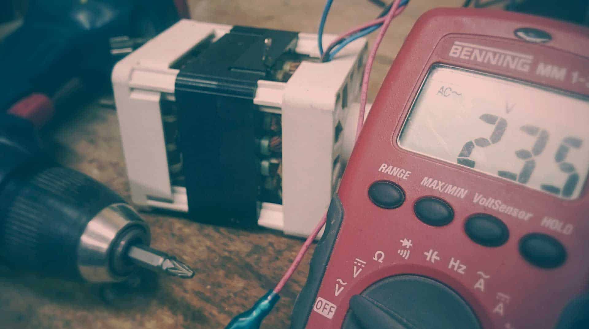 A multimeter and a drill on a workbench.